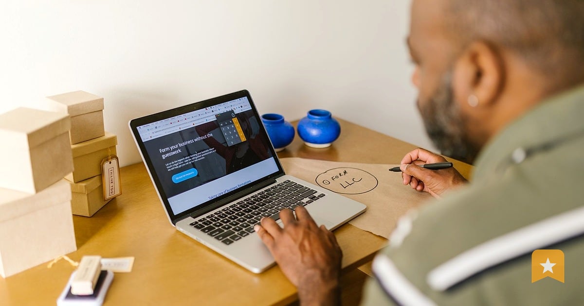 Small business owner at wooden desk reviewing Google Business profile on laptop, considering review strategy for his shop