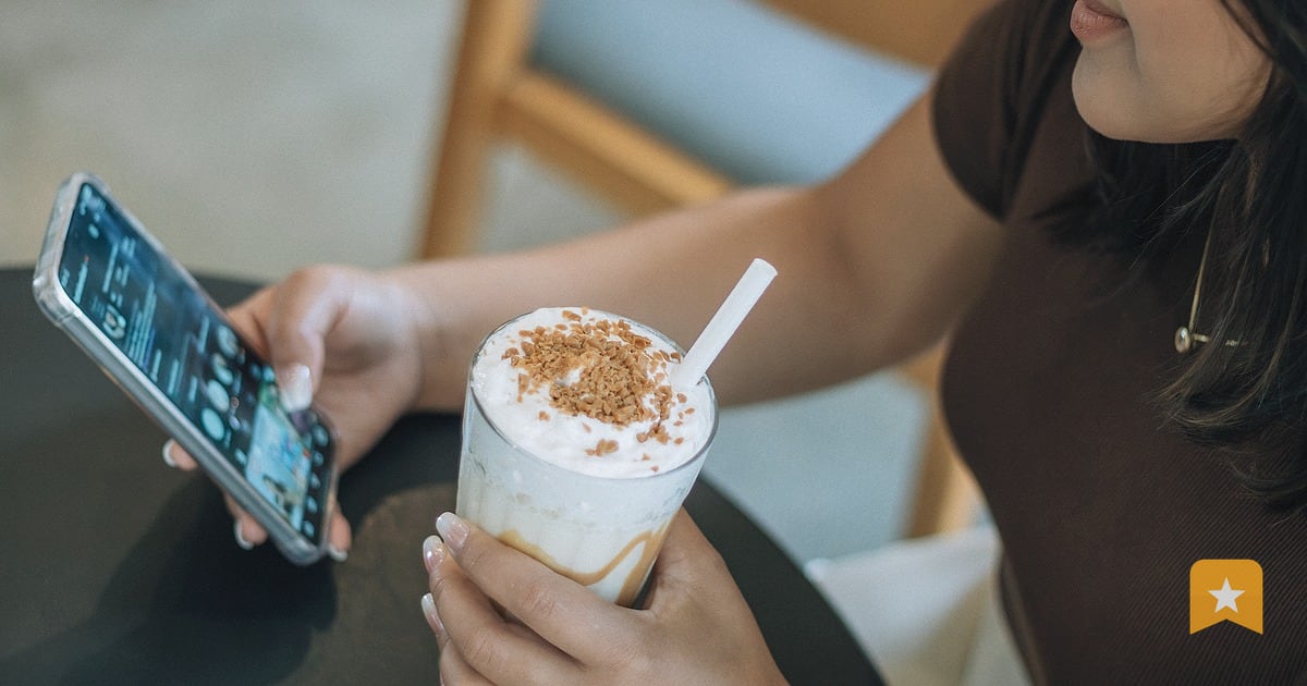 Woman at a cafe holding a phone in one hand and an iced coffee in the other