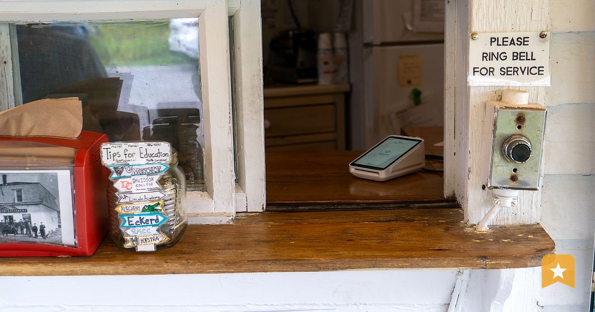 Small-business counter window with a smartphone sitting on the wooden sill, where customers naturally see it after a transaction