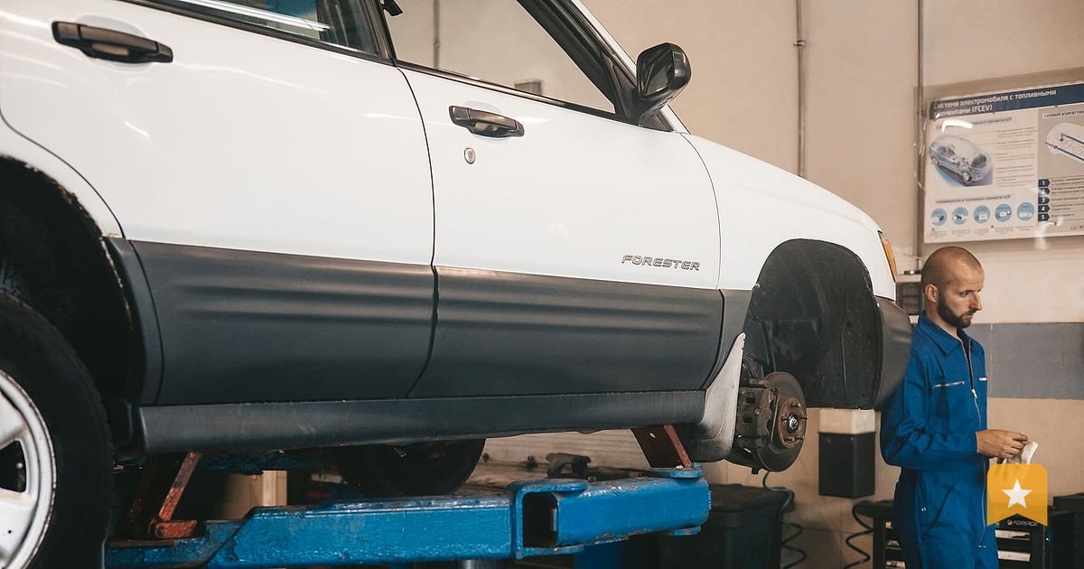 Mechanic in blue coveralls stands beside a car on a lift in a garage workshop