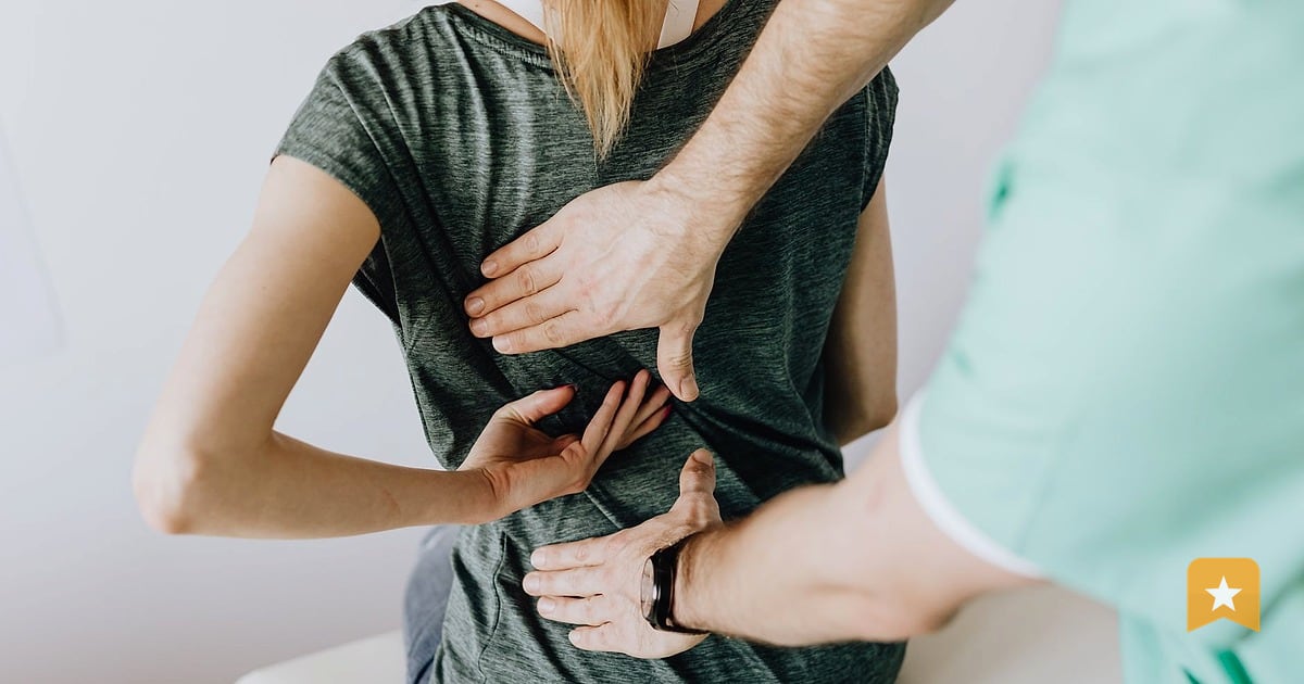 Chiropractor in green scrubs adjusting patient's lower back while she sits on treatment table