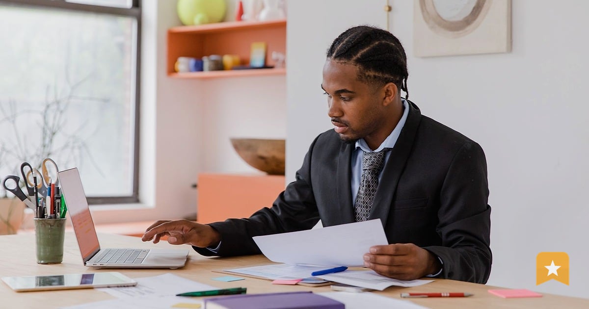 Small business owner at desk reviewing documents and laptop, managing online reputation and customer feedback