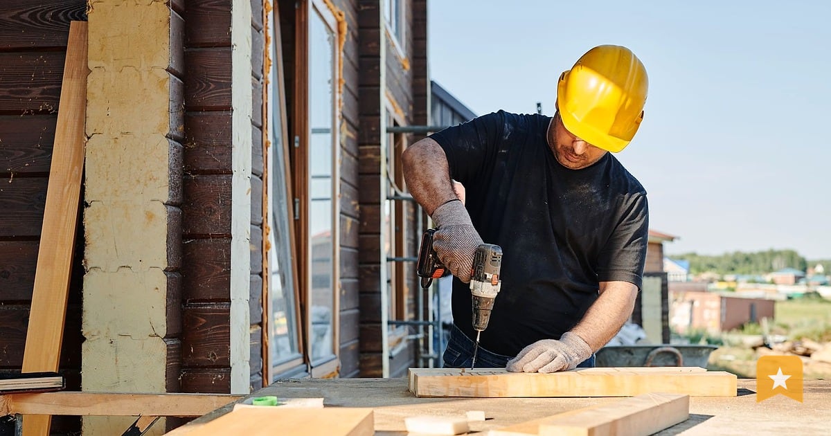 Contractor in yellow hard hat drilling into wood on a sunny job site, the work that drives customer calls and reviews