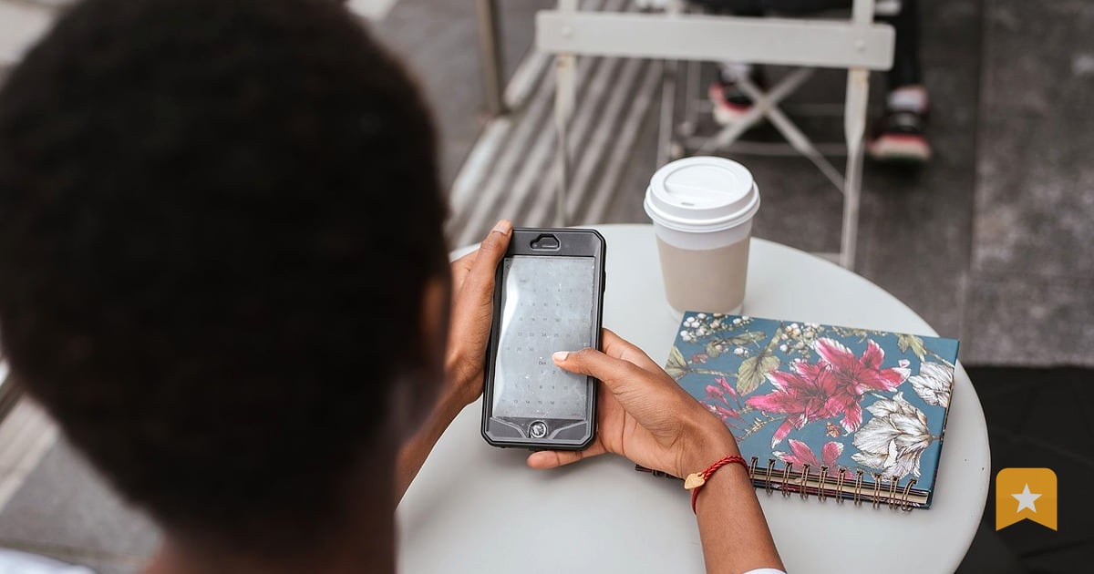 Person holding a phone at a small outdoor cafe table with coffee and notebook nearby